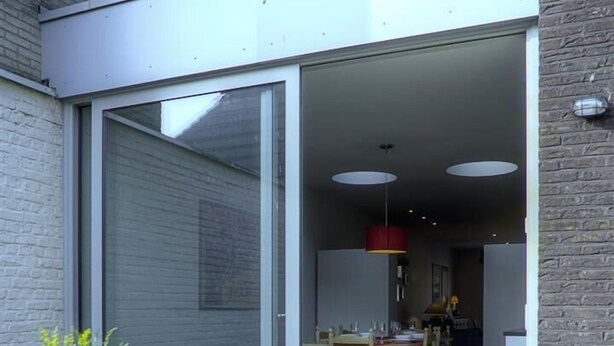 An outdoor patio with a table and chairs, a potted plant, and a sliding glass door leading to an interior dining area. - Menin Gate House 2 (Ypres)