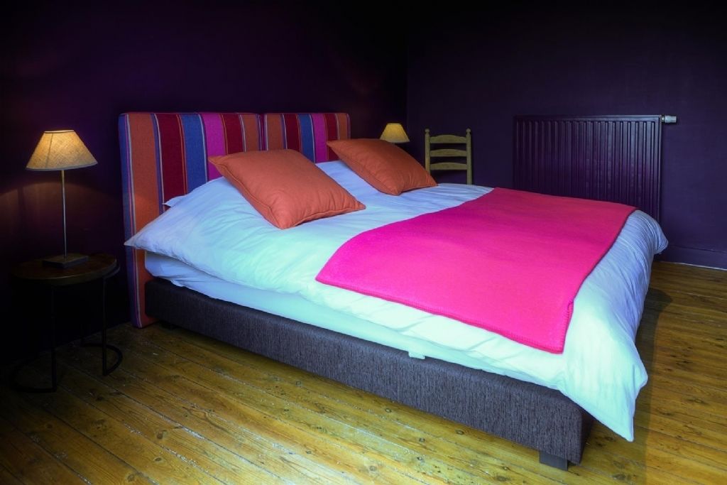 A bed with a colorful striped headboard, two pillows, and a bright pink blanket.