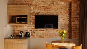 A kitchen with a brick wall, wooden cabinets, a microwave, a coffee maker, and a vase with flowers on a wooden table. - SleepWell Apartments Ordynacka (Warsaw)