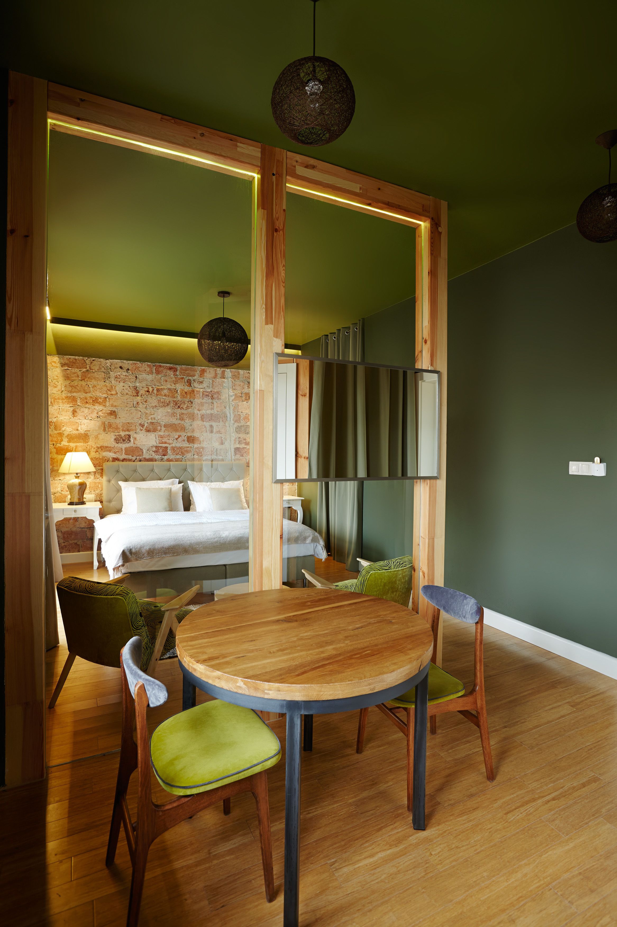 Une chambre moderne avec un lit, une table à manger et des chaises. Un mur de briques se trouve derrière le lit et un mur vert sur le côté.