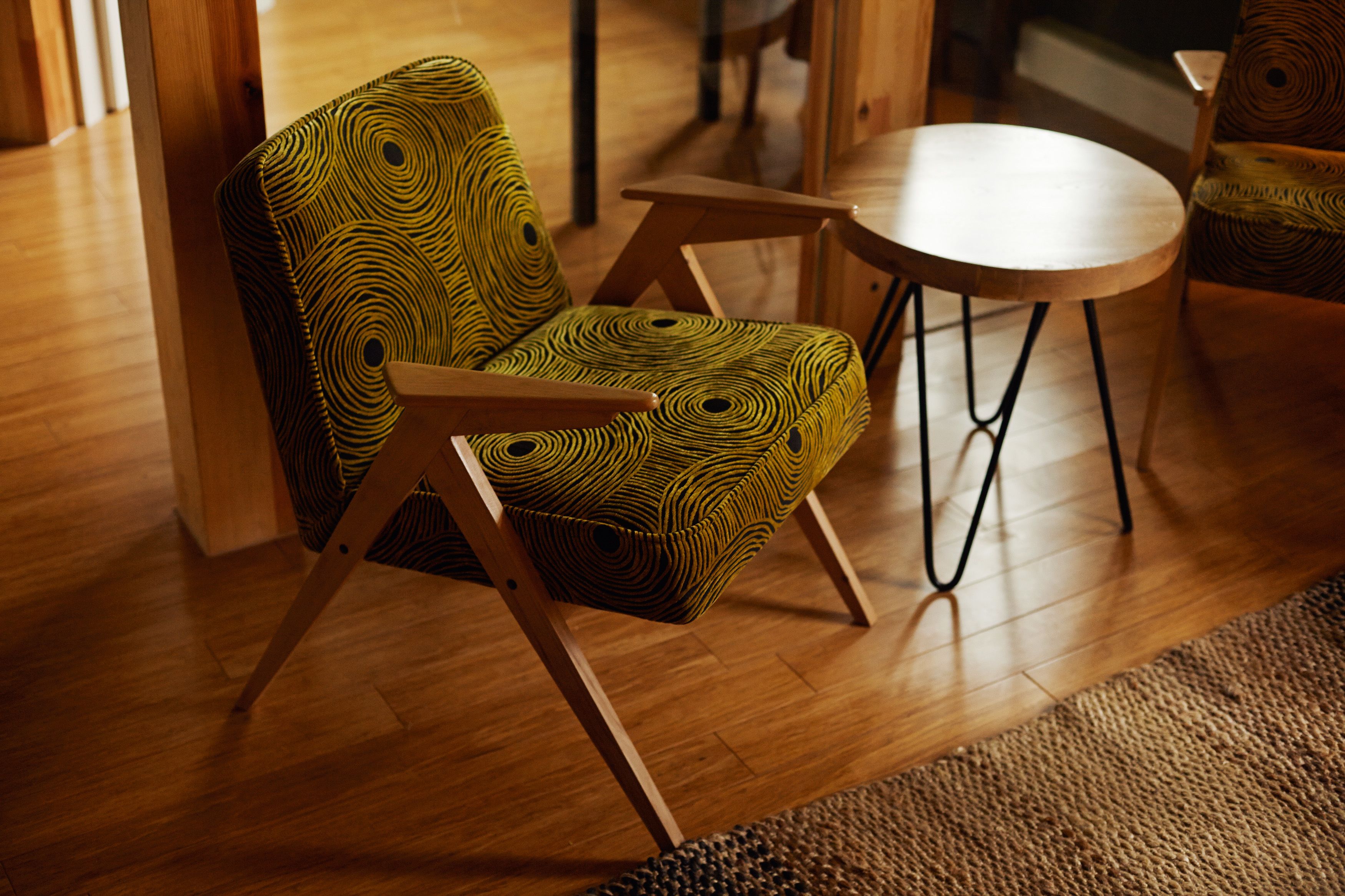 A chair with a geometric pattern, a round wooden table, and wooden flooring.
