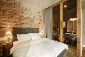 A bedroom with a brick wall, a large bed, two bedside lamps, and a sliding glass door leading to a bathroom.