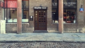 A building with a brick facade, a central entrance with a glass door, and signage for 'SleepWell Apartments' and 'CHolewinski Galanteria Skórzana'. - SleepWell Apartments Ordynacka (Warsaw)