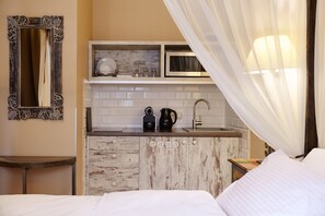 Habitación de hotel pequeña con kitchenette, una cama, una mesita de noche, un espejo y una cortina.