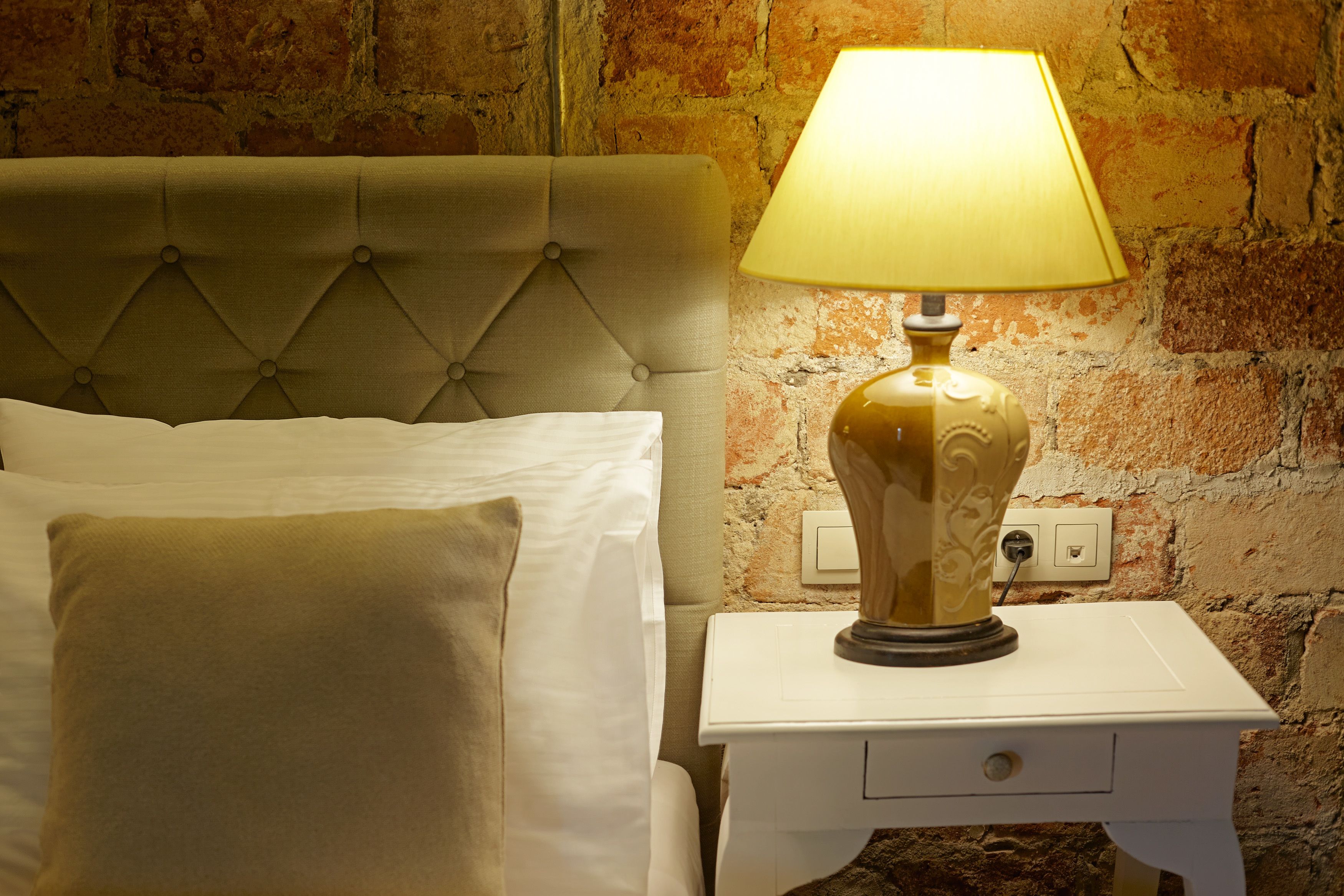 A bed with a tufted headboard, a bedside lamp, and a white nightstand with a drawer.
