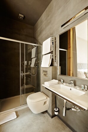 Un baño moderno con ducha de vidrio, inodoro blanco y un espejo grande sobre el lavabo.