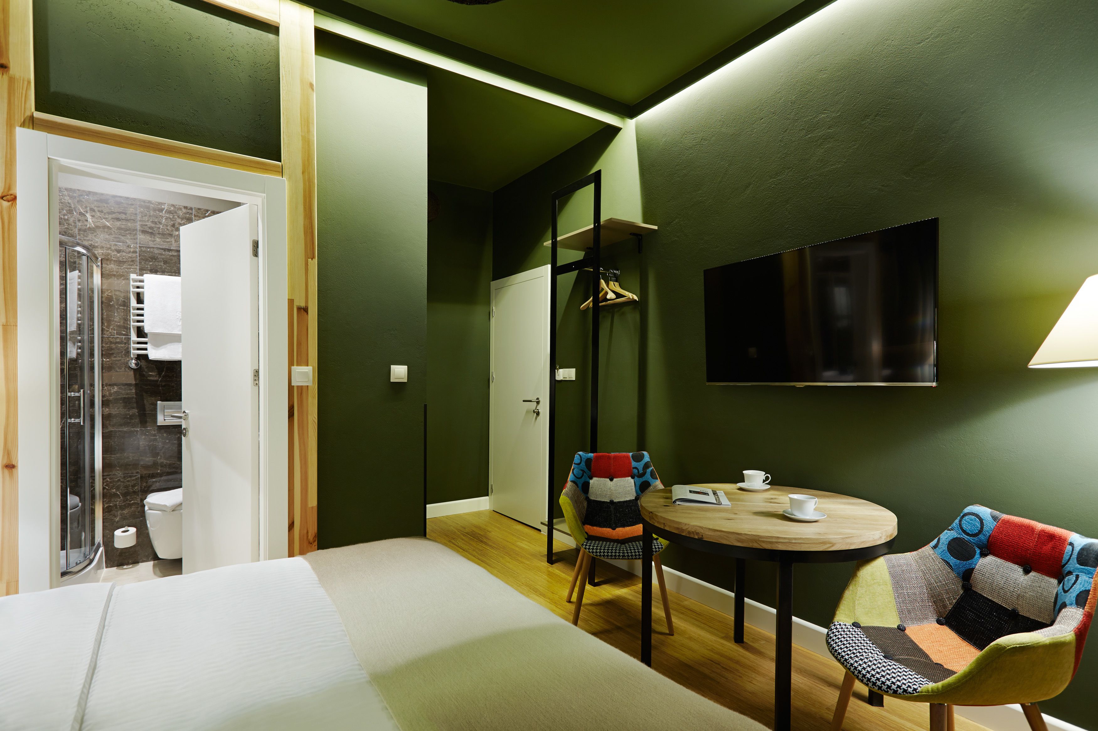 A room with a bed, a round table with two chairs, a TV mounted on the wall, and a door leading to a bathroom.
