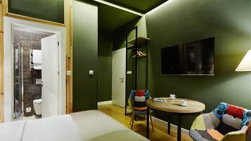 A room with a bed, a round table with two chairs, a TV mounted on the wall, and a door leading to a bathroom.