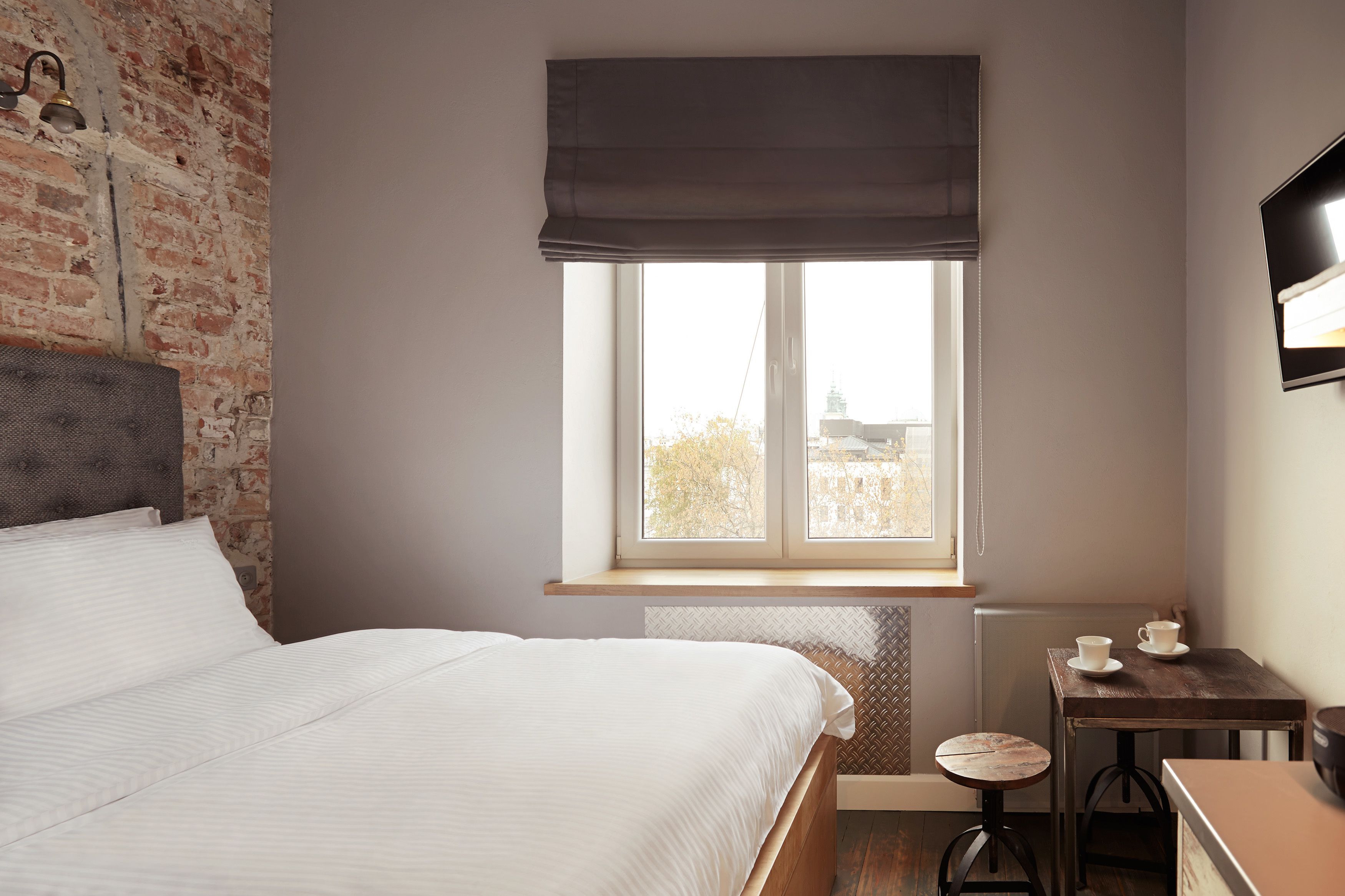 Un dormitorio con una cama, un ventanal con vistas, una mesita con tazas y una pared de ladrillo.