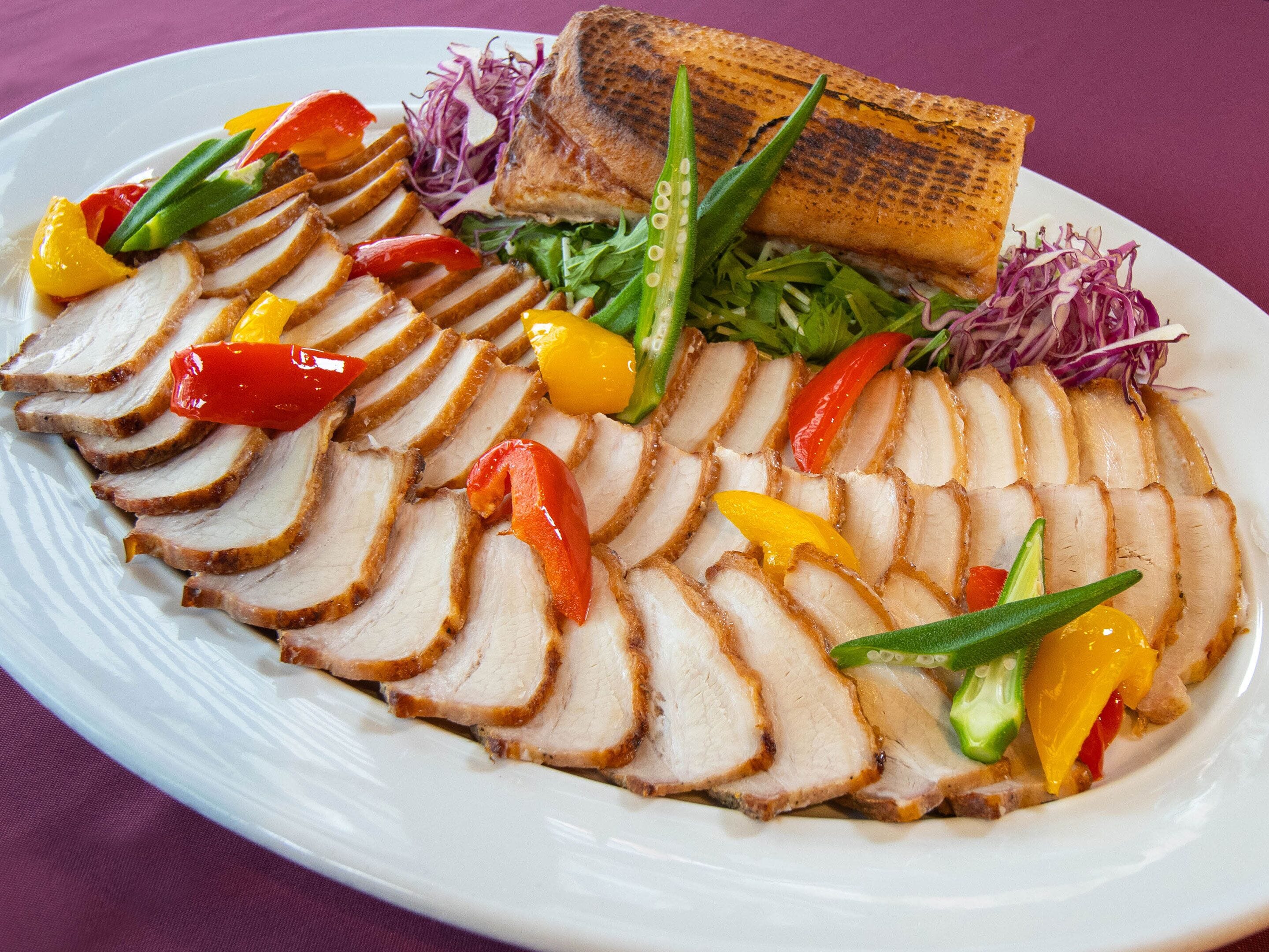 A plate of sliced roasted pork with vegetables and a piece of bread.