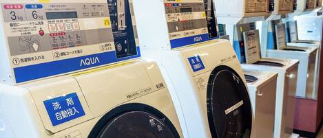 A row of front-loading washing machines with control panels and labels in a commercial setting.