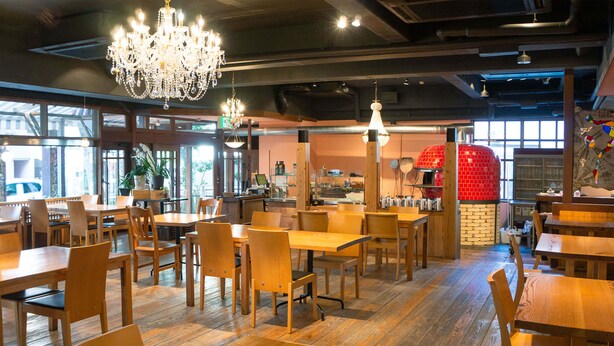 A restaurant interior with wooden tables and chairs, a chandelier, and a red brick oven. - APA Hotel Kochi (Kochi)
