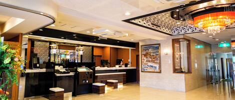 A hotel lobby with a reception desk, seating area, and a large chandelier.