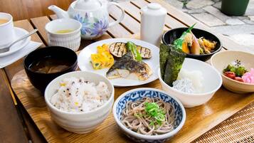 A wooden table with various dishes including rice, noodles, and grilled fish, along with a teapot and cups.