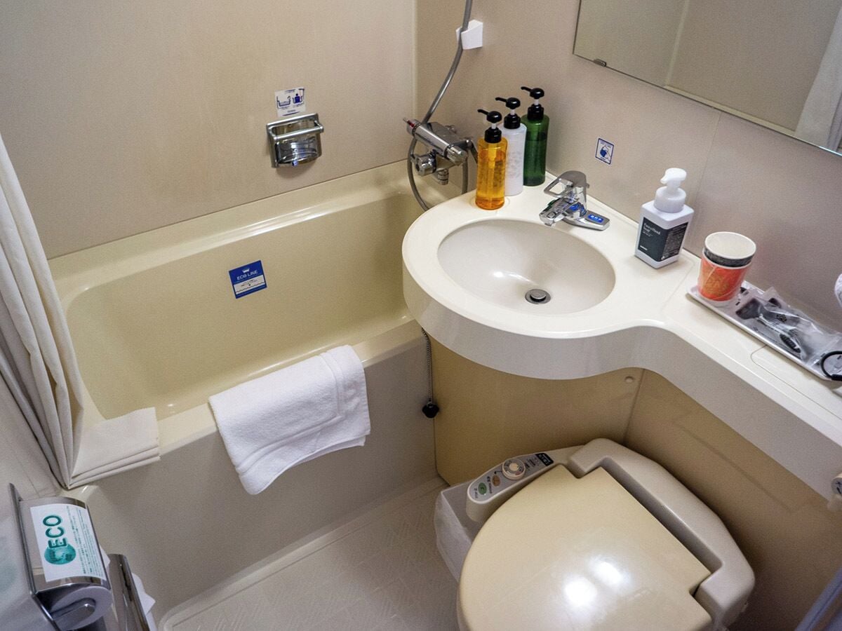 A bathroom with a bathtub, a sink, and a toilet. There are toiletries on the sink and a towel hanging on the wall.