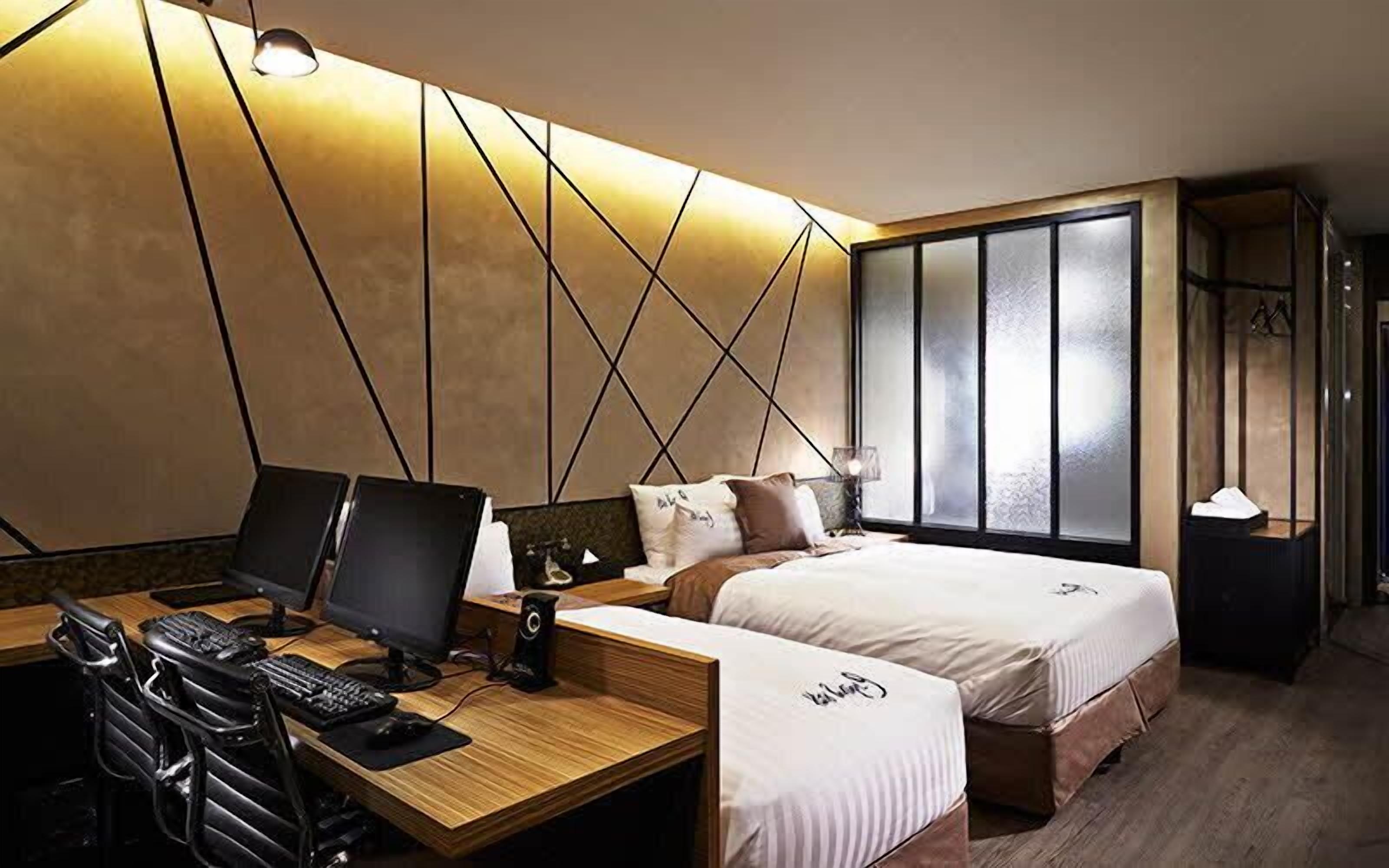 Une chambre d’hôtel moderne avec un bureau en bois, deux lits et une grande fenêtre dotée de panneaux en verre dépoli.
