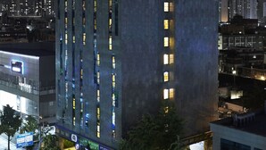 Un hotel moderno con un cartel iluminado llamativo, varios pisos y un área de entrada bien iluminada.