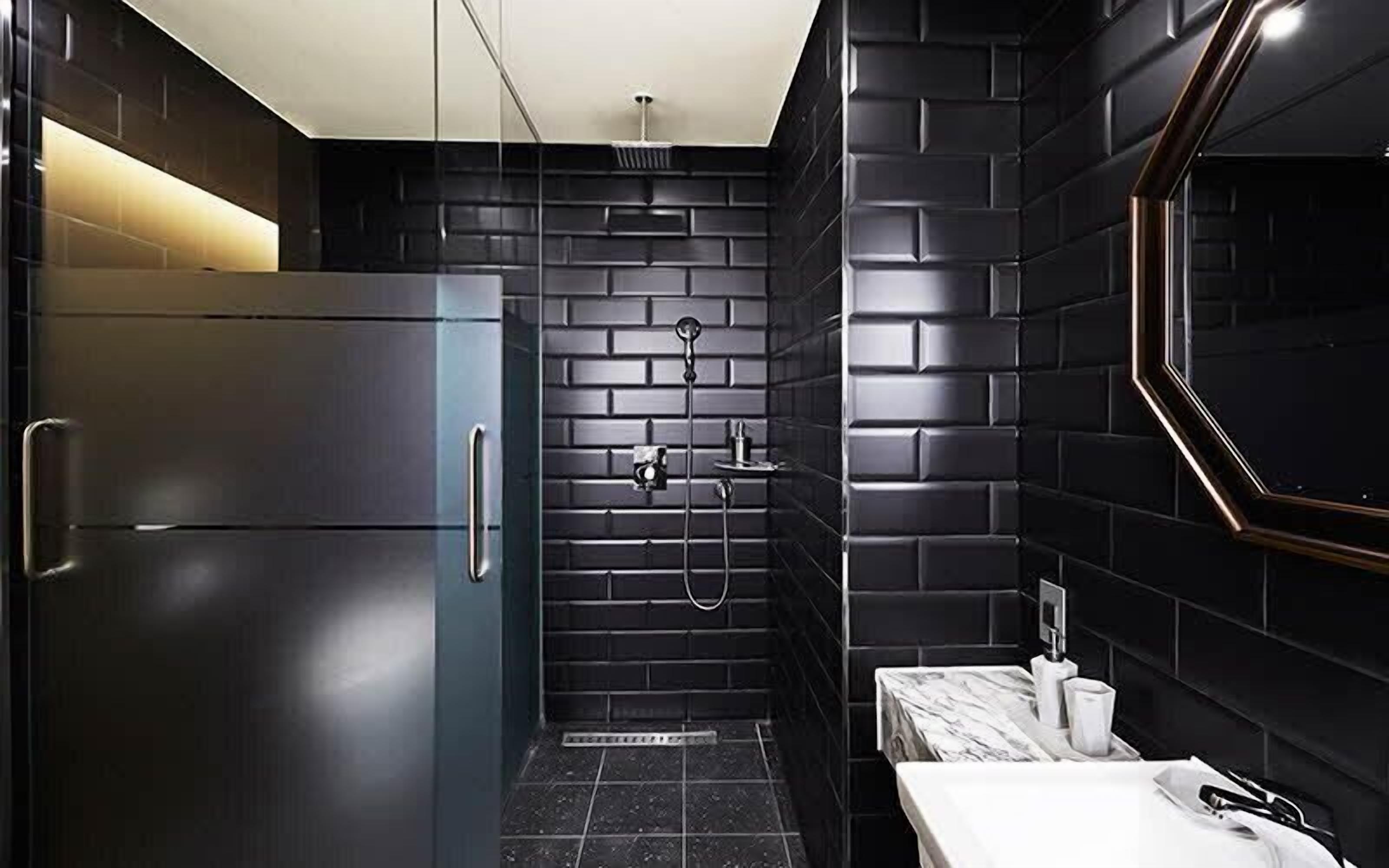 A modern bathroom with a black tiled shower, a marble countertop, and a stainless steel refrigerator.