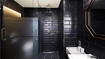 A modern bathroom with a black tiled shower, a marble countertop, and a stainless steel refrigerator.