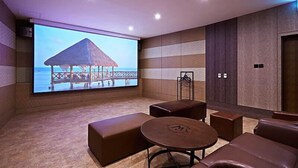 Un área de descanso moderna con una gran pantalla que muestra una playa tropical, asientos acolchados y un diseño minimalista.