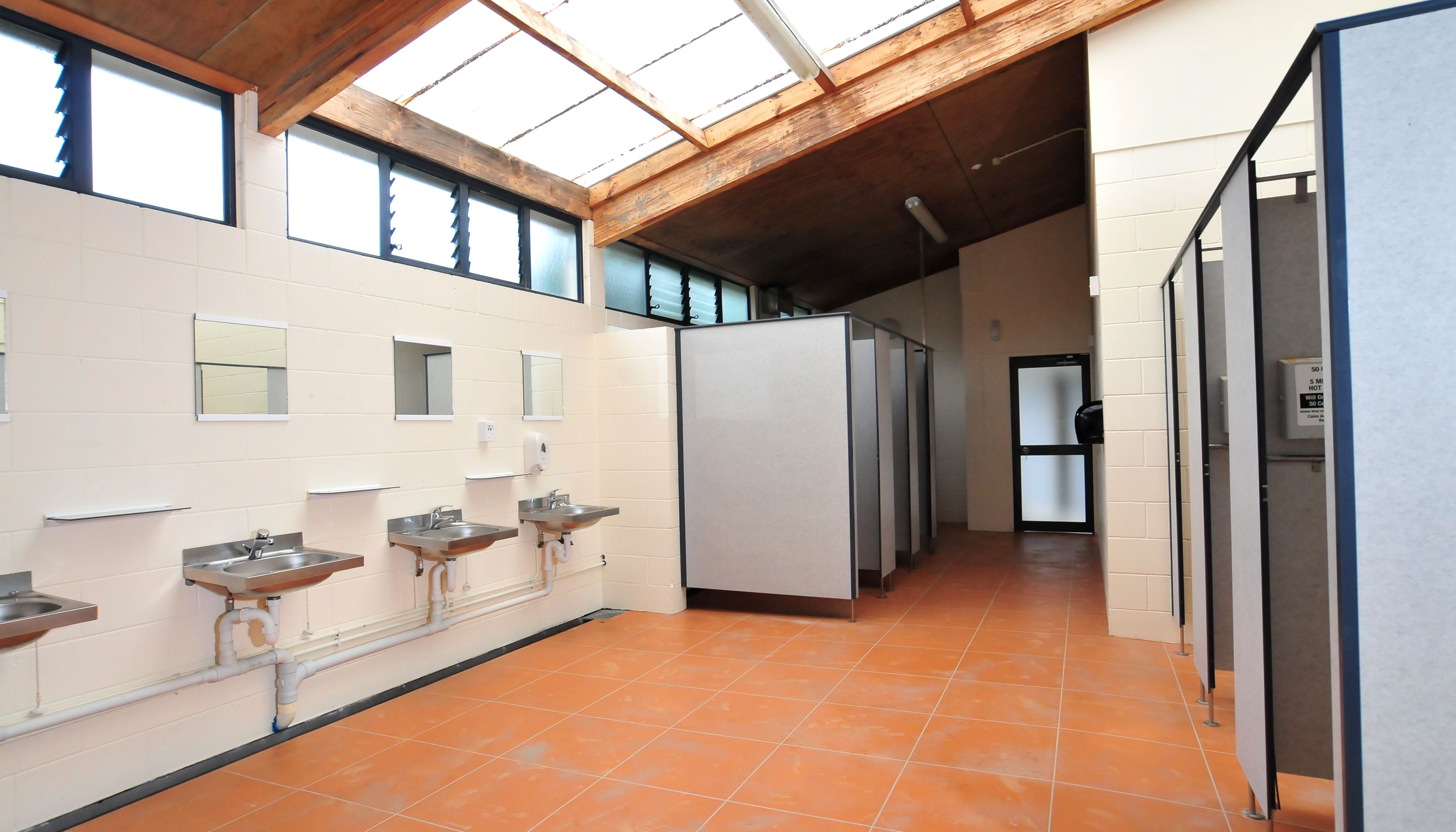 Un baño público con tres lavamanos, un secador de manos y un refrigerador.