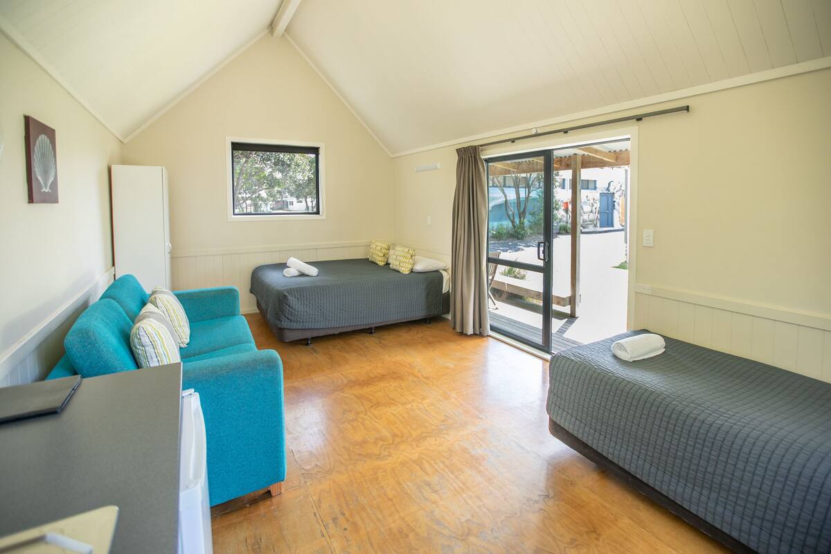 A room with a wooden floor, a sofa, a bed, and a window.