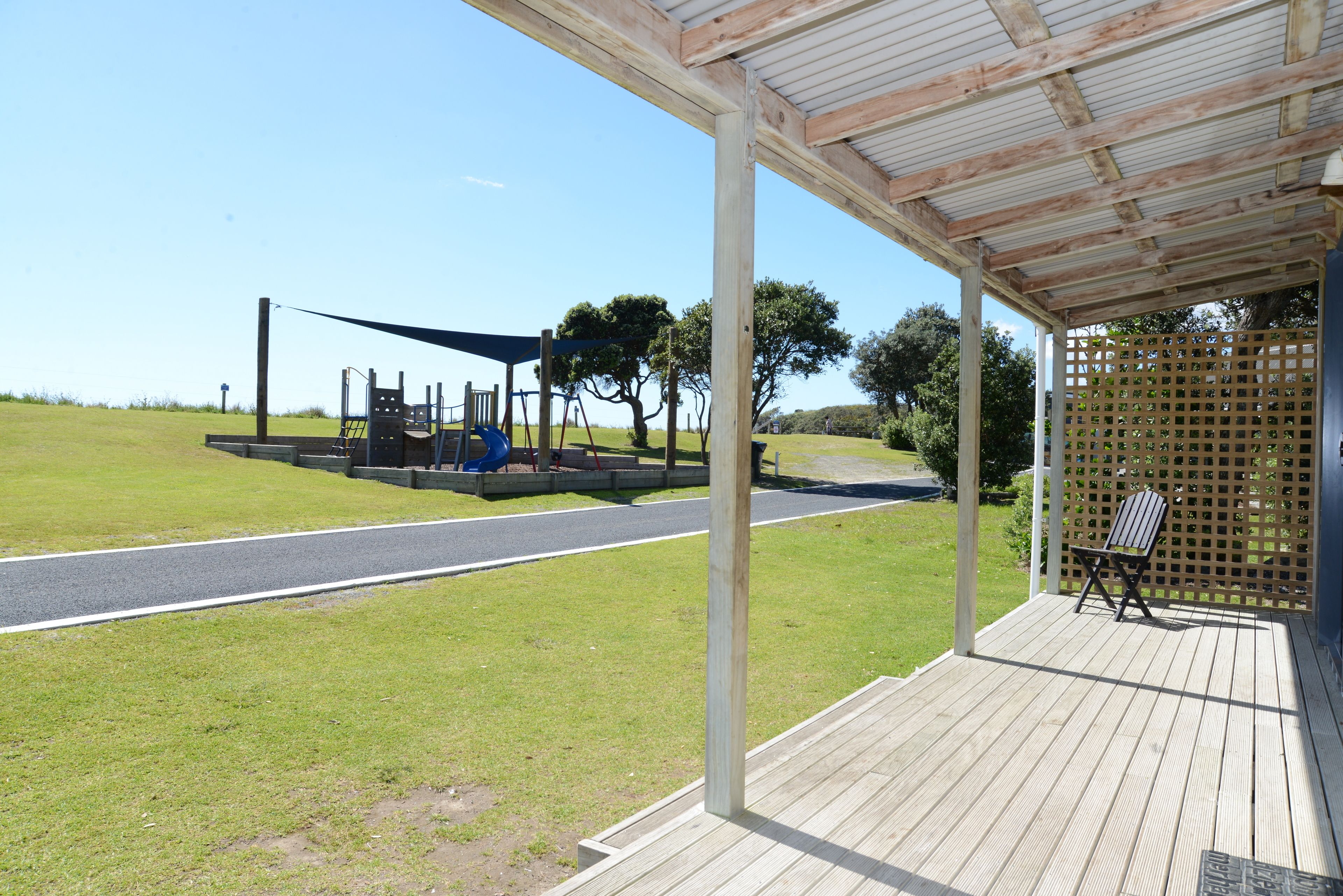 Un espace extérieur abrité doté d’une terrasse en bois, d’une aire de jeux avec un toboggan et d’un coin salon avec une chaise.