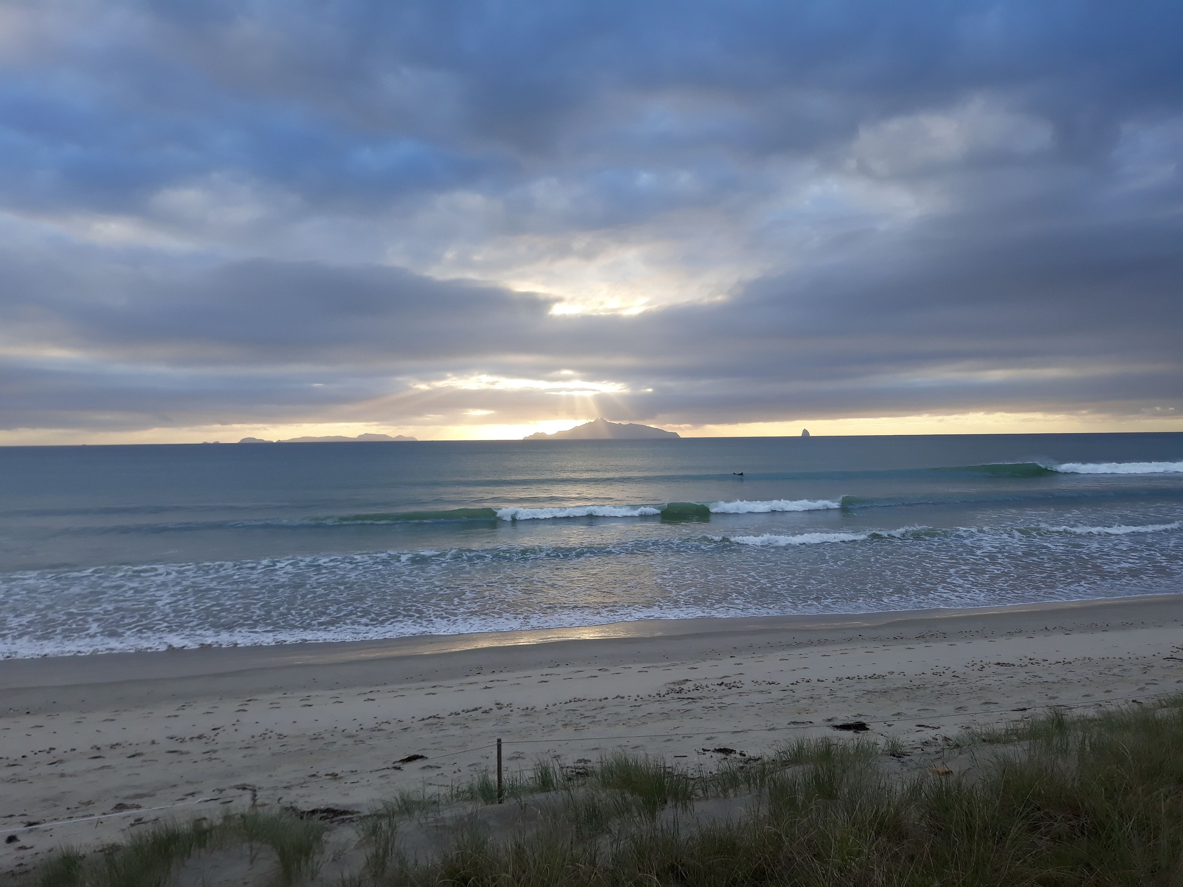 Une plage avec des vagues, un rivage sablonneux et un ciel nuageux.