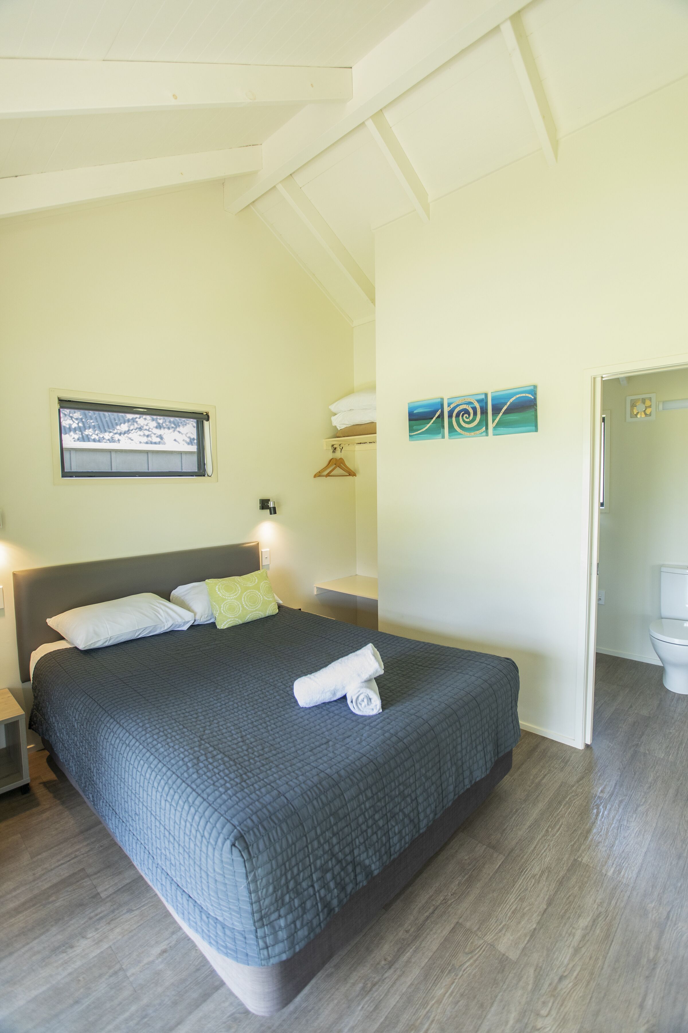 A bedroom with a large bed, a window, and a painting on the wall.