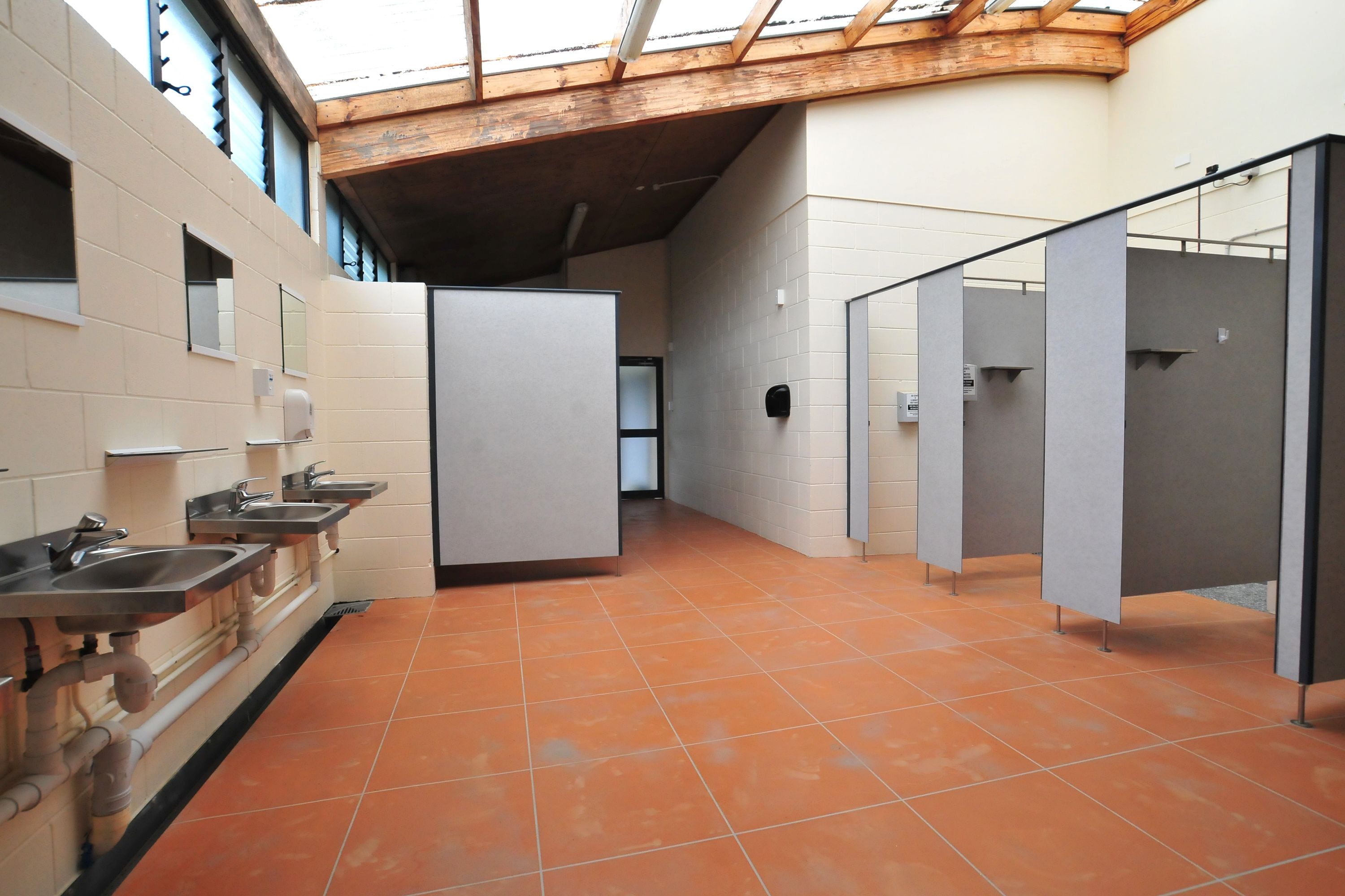 Eine öffentliche Toilette mit mehreren Waschbecken, einzelnen Kabinen und einem gefliesten Boden.
