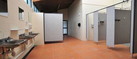 Eine öffentliche Toilette mit mehreren Waschbecken, einzelnen Kabinen und einem gefliesten Boden.