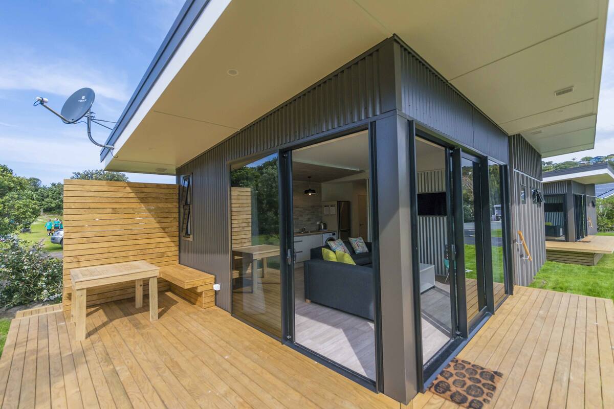 A modern outdoor living space with a wooden deck, a glass door leading to a kitchen area, and a satellite dish.