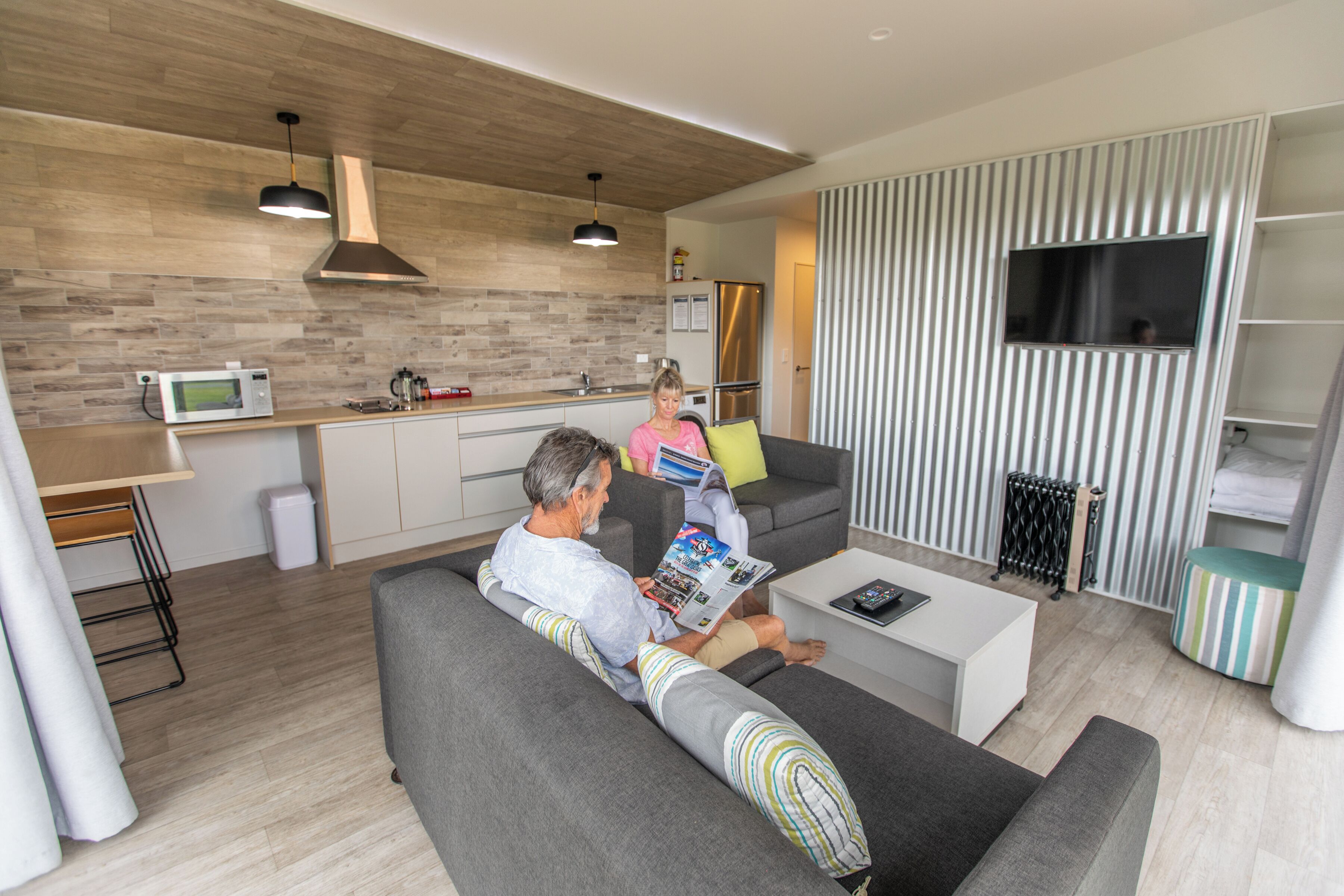 A modern living room with a grey sofa, a coffee table, and a TV mounted on a striped wall.