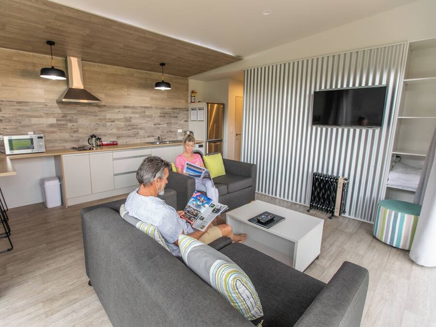 A modern living room with a grey sofa, a coffee table, and a TV mounted on a striped wall.