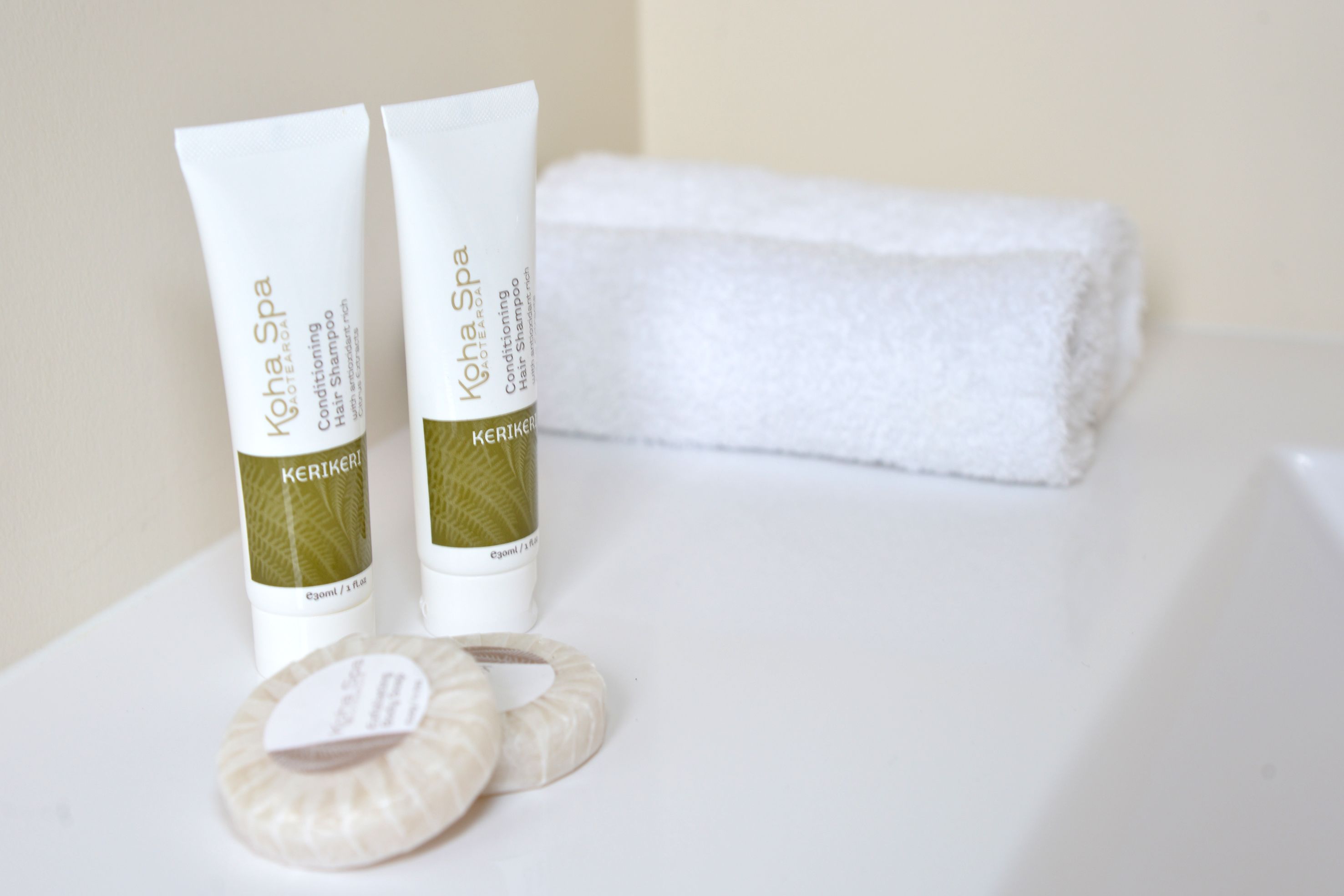 Twee tubes KOHA Spa conditioner shampoo en twee ronde, witte badsponges op een wit oppervlak.
