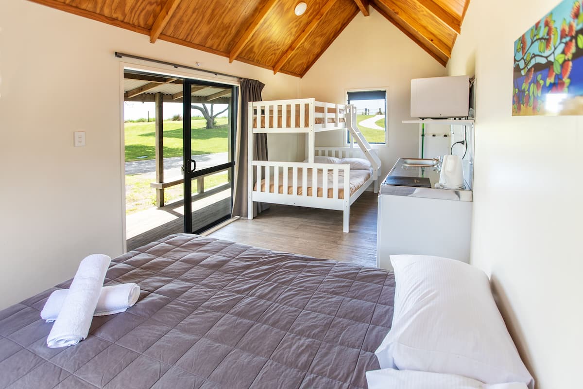 A bedroom with a bunk bed, a desk with a computer, and a window with a view of a green landscape.