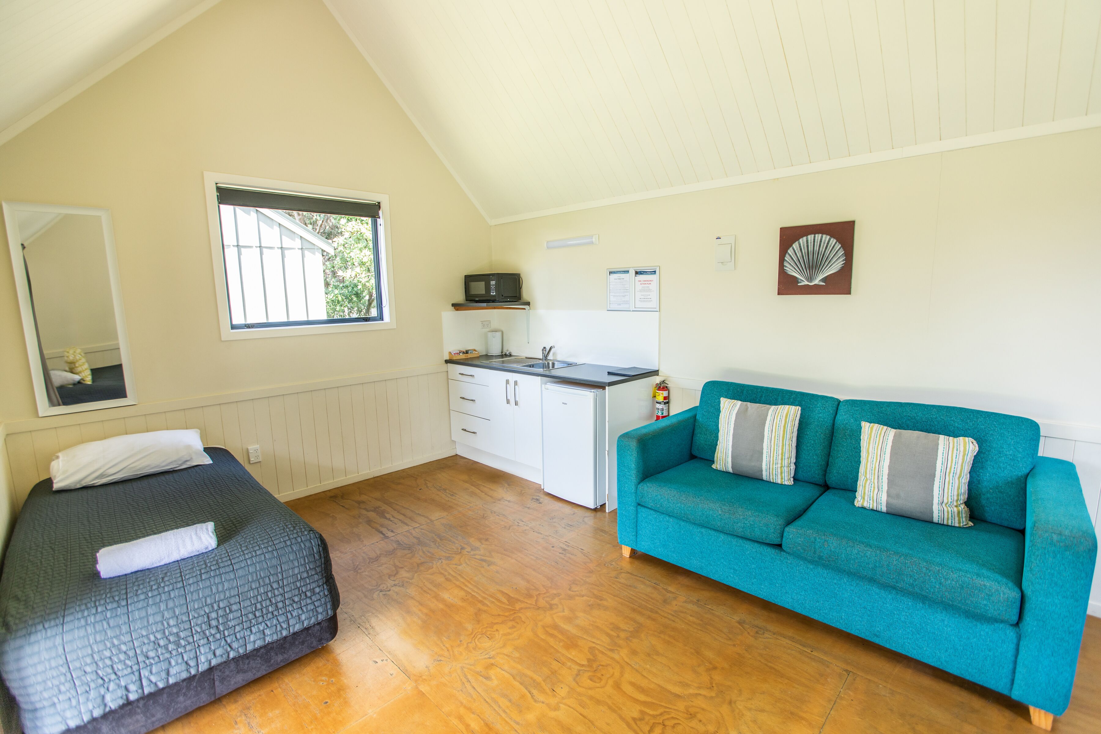 A room with a bed, a sofa, a kitchenette, and a window.