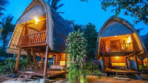 Two thatched-roof cottages with wooden balconies, surrounded by tropical vegetation. - Sukanusa Luxury Huts (Lembongan Island)