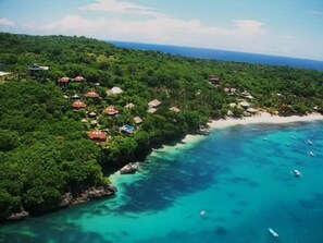 Vue aérienne d’une station balnéaire avec des bungalows sur pilotis, une eau turquoise cristalline et une plage.