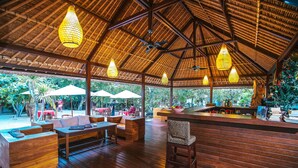 An outdoor wooden deck with seating, a bar area, and a thatched roof structure. - Sukanusa Luxury Huts (Lembongan Island)