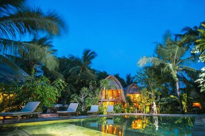 Un complexe hôtelier doté d’une piscine, de chaises longues et d’une végétation tropicale.