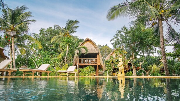 A poolside area with lounge chairs, a thatched-roof structure, and lush tropical vegetation. - Sukanusa Luxury Huts (Lembongan Island)