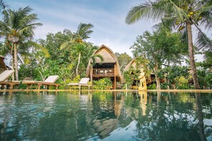 Un espace aménagé au bord de la piscine, avec des chaises longues, une structure à toit de chaume et une végétation tropicale luxuriante.