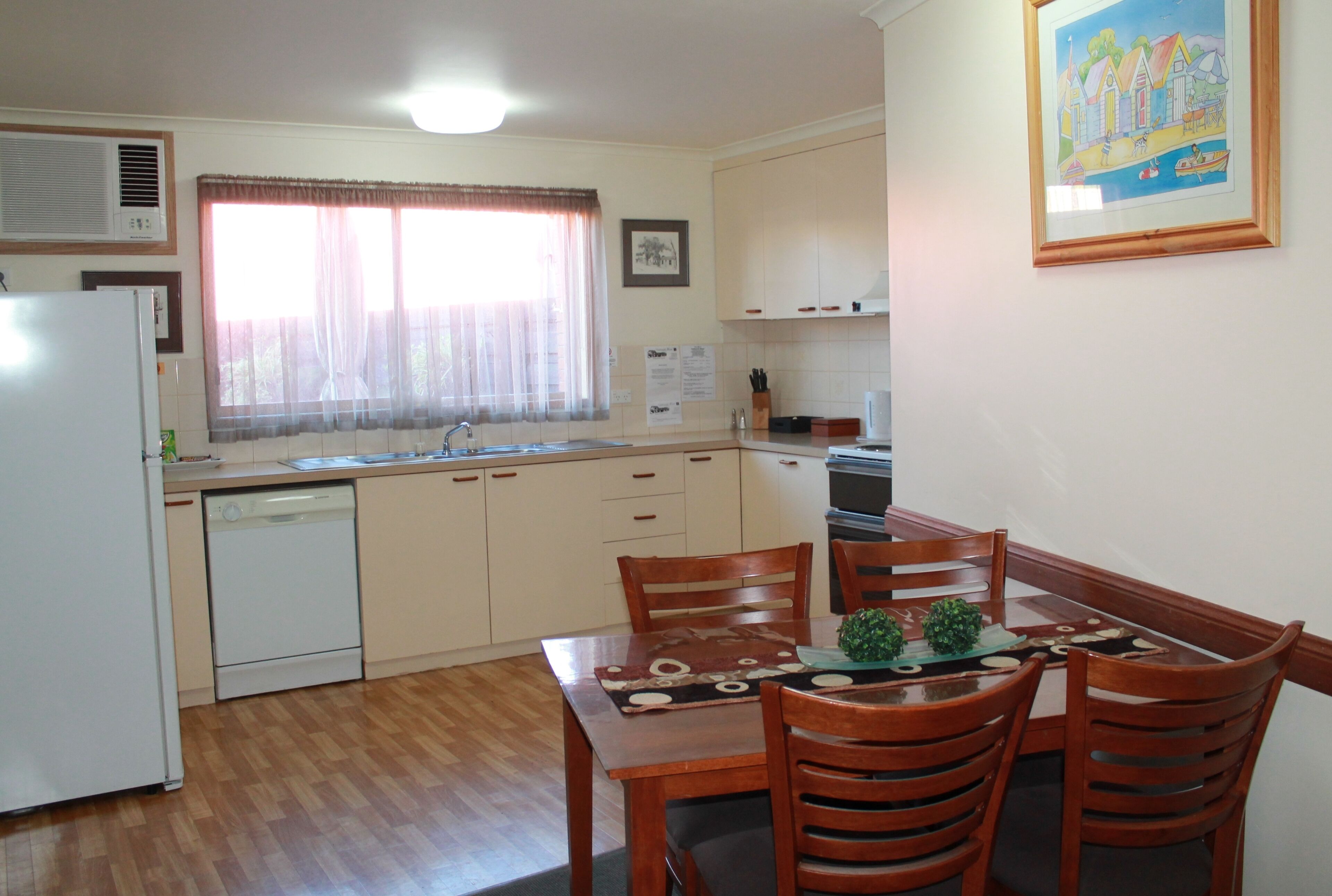 A compact kitchen with a refrigerator, dishwasher, and a dining area with wooden chairs and a table.