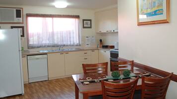 A compact kitchen with a refrigerator, dishwasher, and a dining area with wooden chairs and a table.