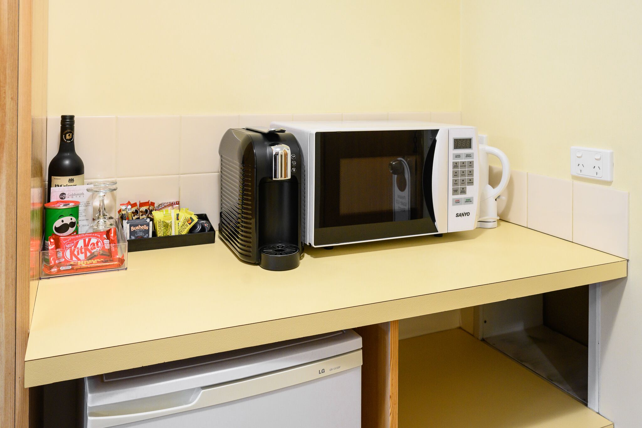Uma cozinha equipada com micro-ondas, máquina de café e pequena geladeira.