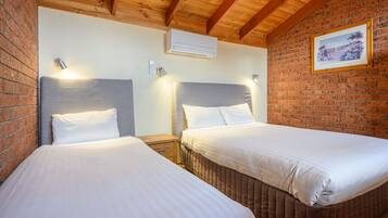 Una habitación con dos camas, una pared de ladrillo y un cuadro enmarcado.