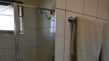 Une salle de bain avec une douche, un lavabo équipé de produits de toilette et des serviettes accrochées au mur.