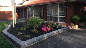 A two-story house with a red roof, large windows, and a landscaped garden with pink flowers.