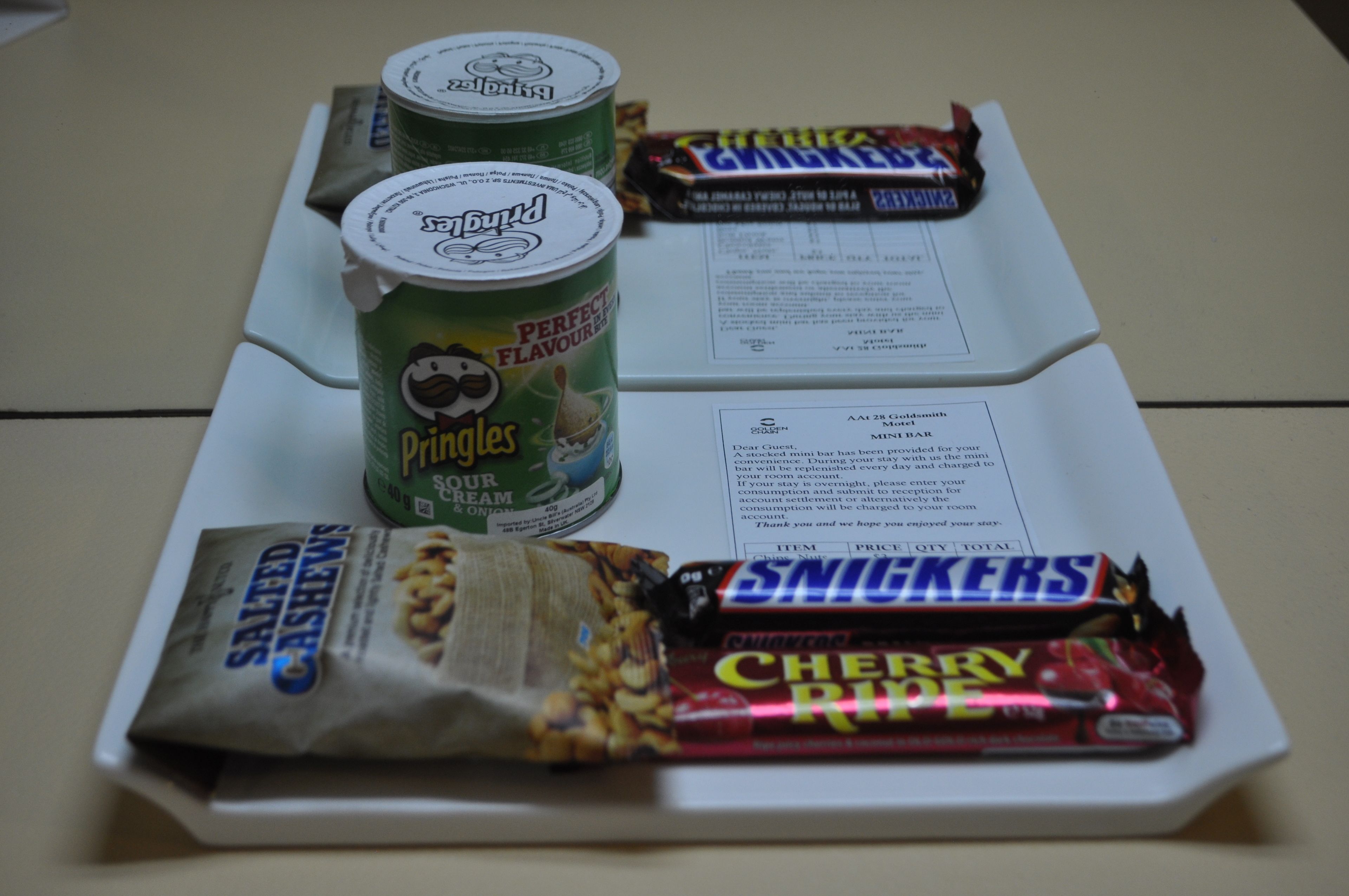 Ein Tisch mit einer Speisekarte, zwei Dosen Pringles, einer Snickers-Riegel und einer Tüte gesalzene Cashewnüsse.